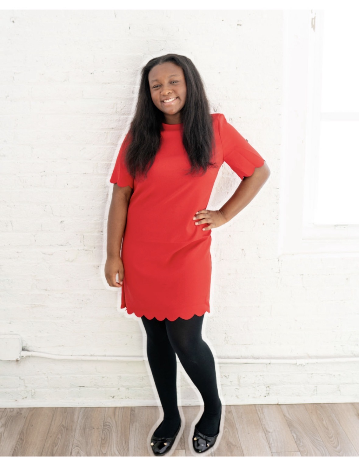 Mya smiling in a red dress in front of a white brick wall